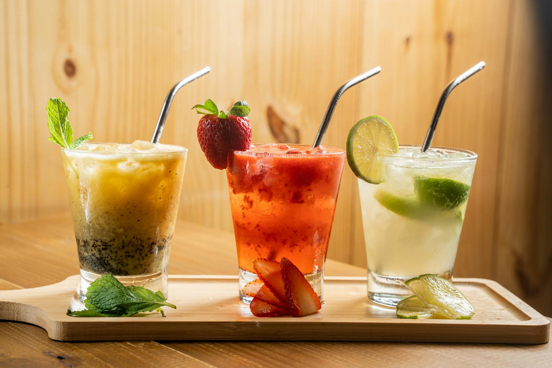 three different drinks on a wooden tray with straws
